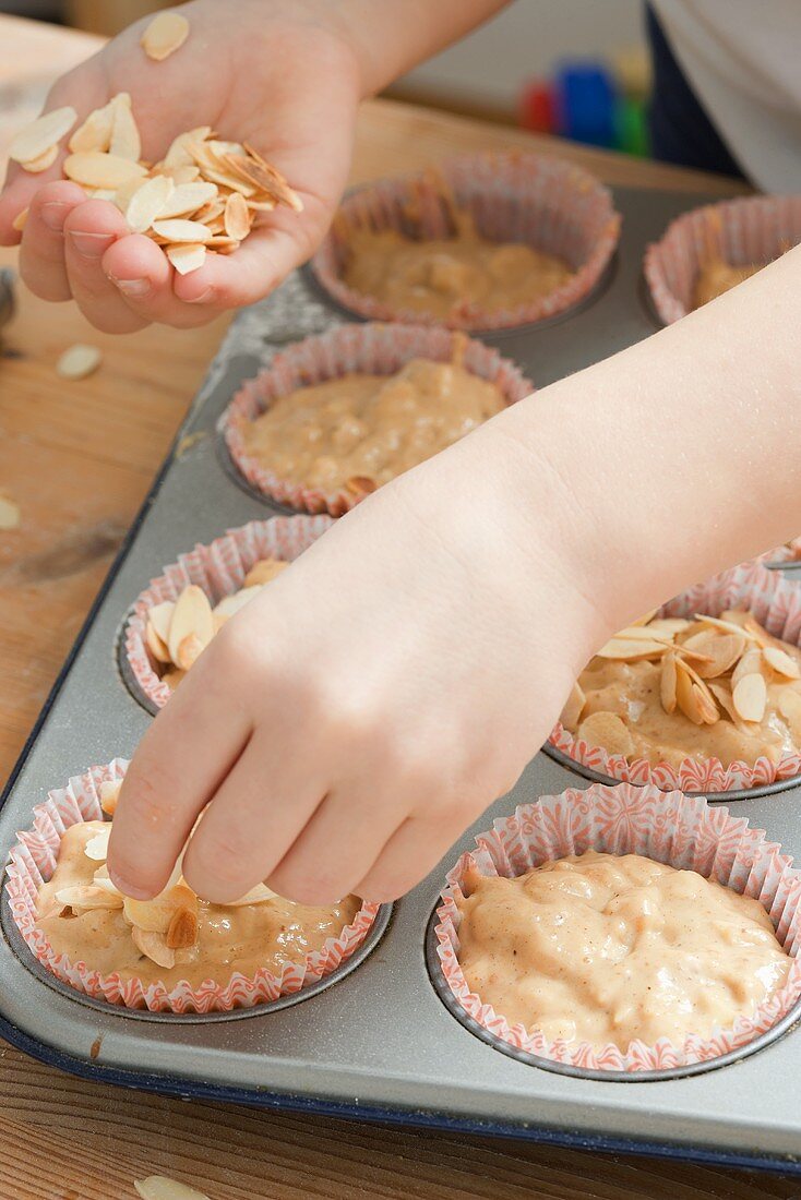 Child sprinkling flaked almonds on unbaked muffins
