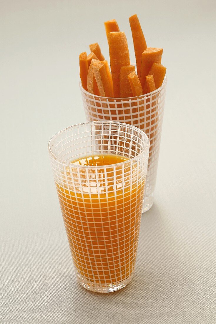 A glass of carrot juice and a glass of carrot sticks