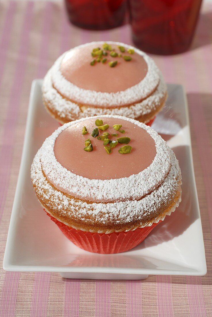 Two pink marzipan muffins with icing sugar and pistachios