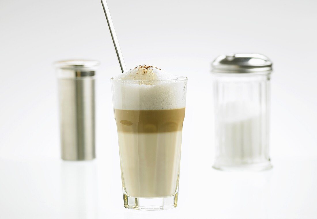 A glass of latte macchiato with sugar and cocoa shakers