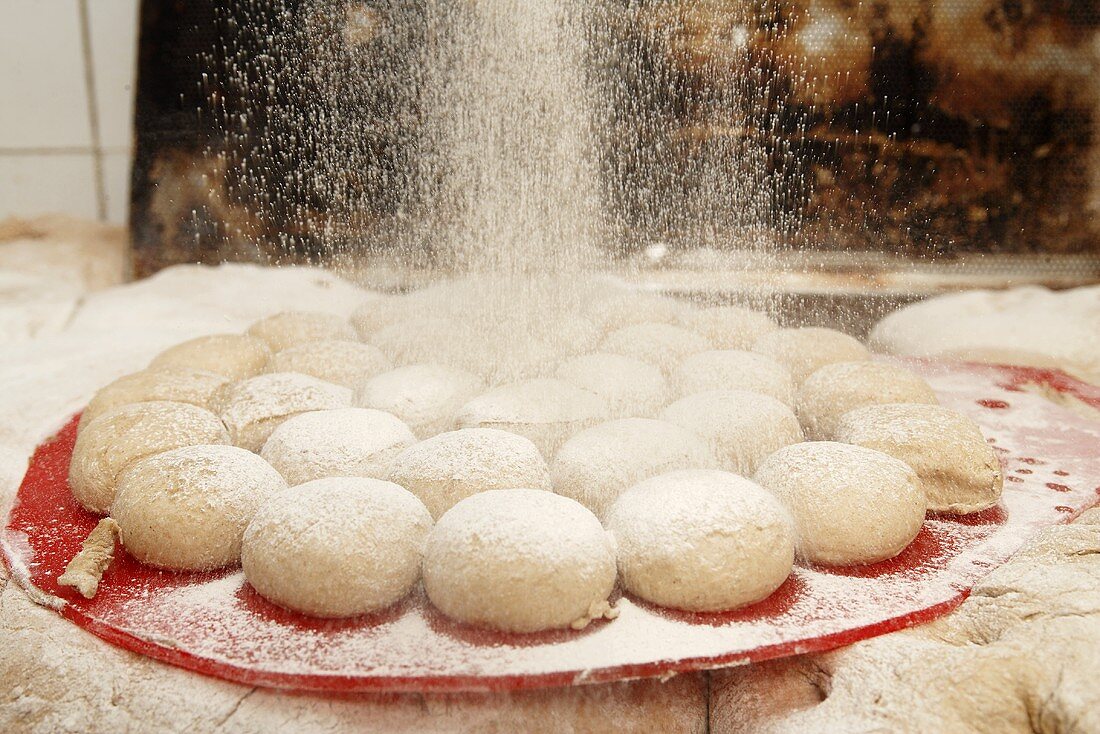 Dusting unbaked bread rolls with flour in bakery