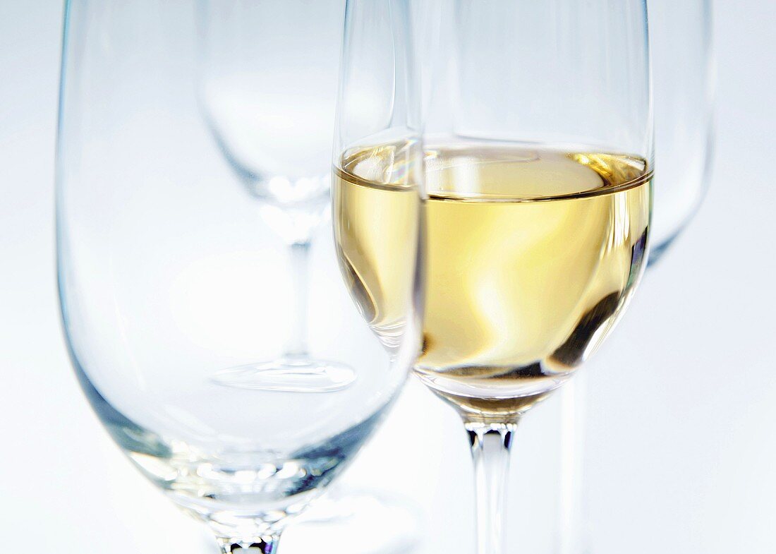 Zwei leere Gläser und ein eingeschenktes Glas Weißwein