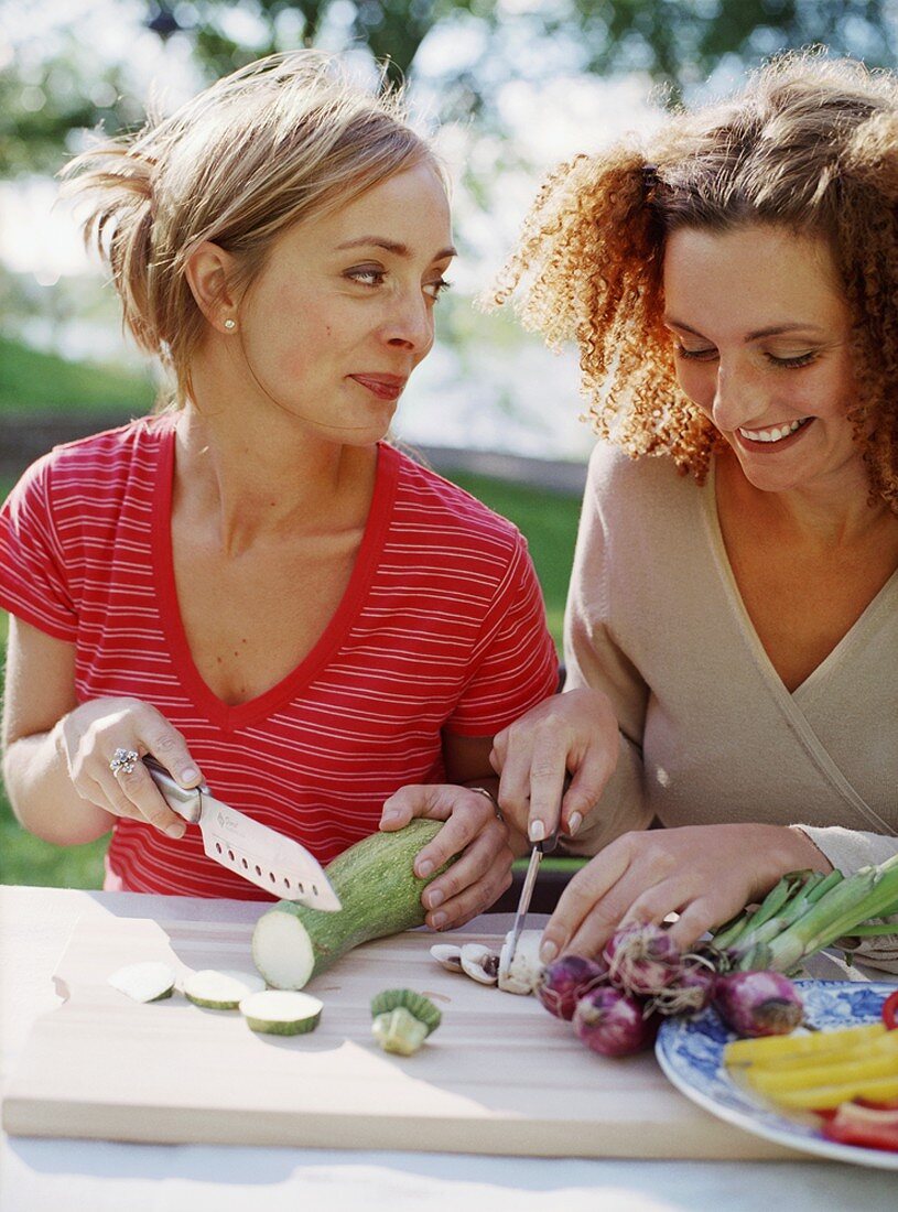 Two women slicing vegetables out of doors