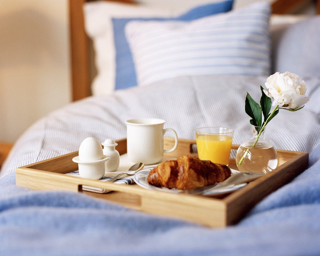 Frühstückstablett mit Croissant, Ei und Saft auf dem Bett
