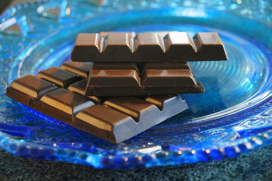 Gebrochene Schokoladentafel auf blauem Glasteller