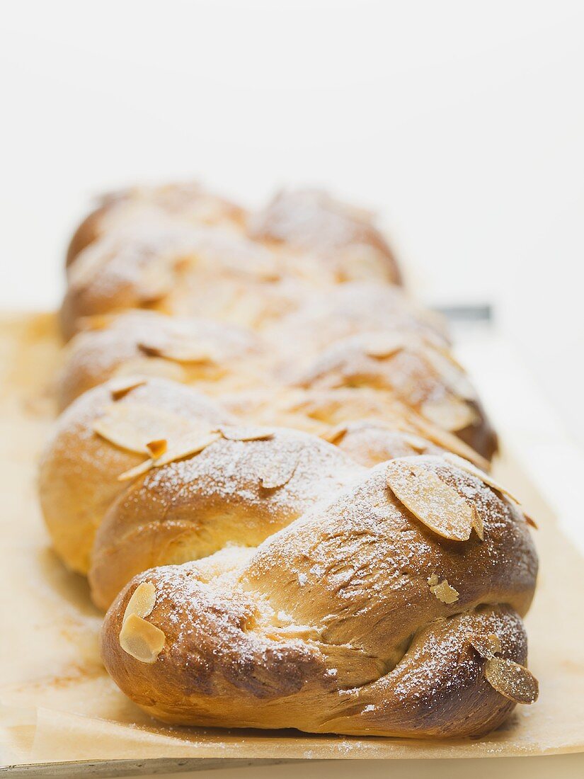 Bread plait with flaked almonds & icing sugar on baking parchment