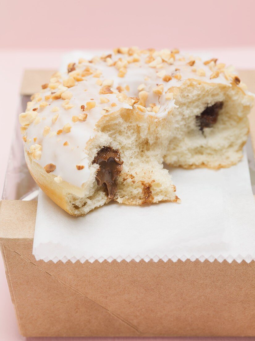 Doughnut mit Schokofüllung, Zuckerglasur und gehackten Nüssen, angebissen