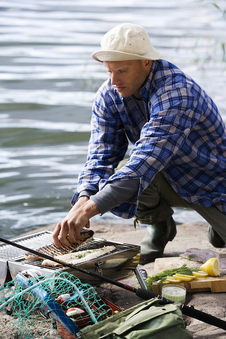 Mann grillt Fisch am Ufer (Schweden)
