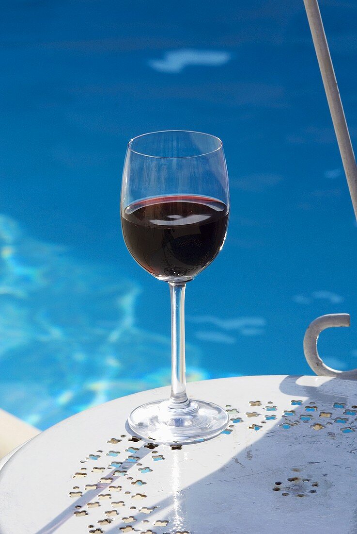 A glass of red wine on a small table by a pool