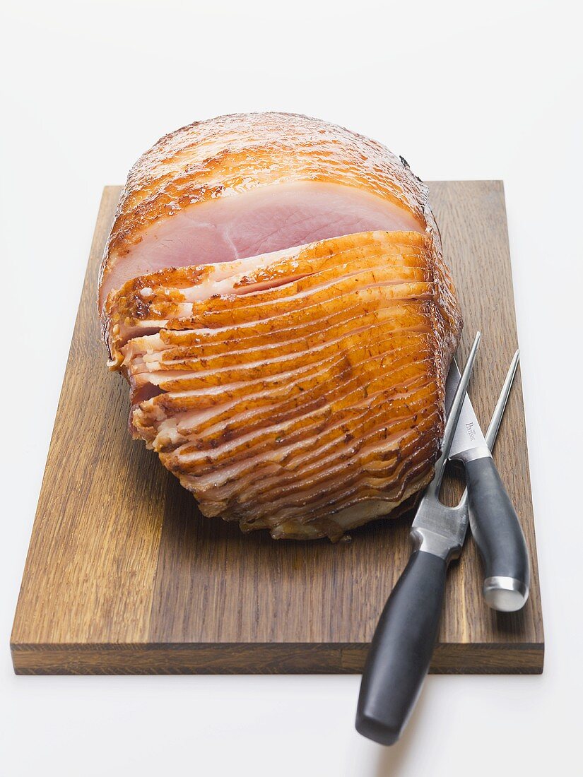 Glazed ham on chopping board with carving cutlery