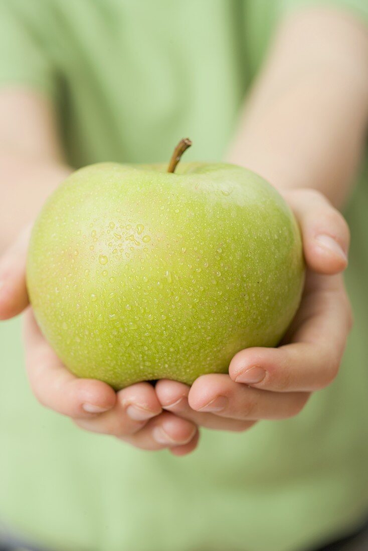 Child holding Granny Smith apple with drops of water