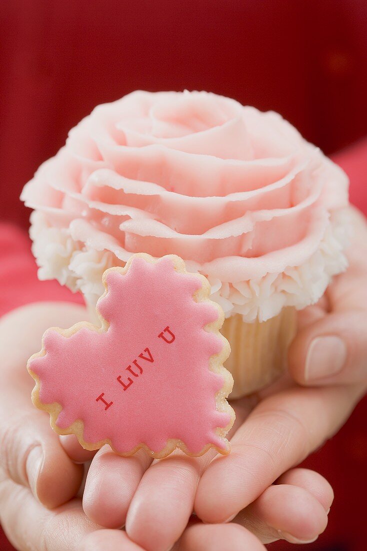 Hände halten Cupcake und Plätzchen zum Valentinstag