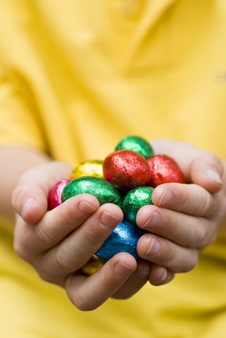 Child's hands holding chocolate Easter eggs in coloured foil