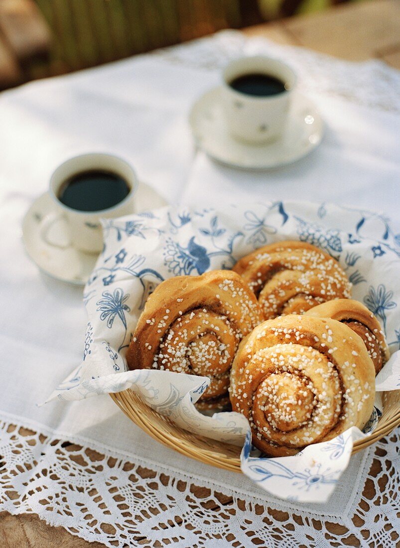 Cinnamon buns in bread basket and two cups of coffee