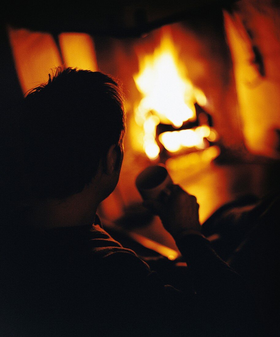 Man with cup sitting in front of fire