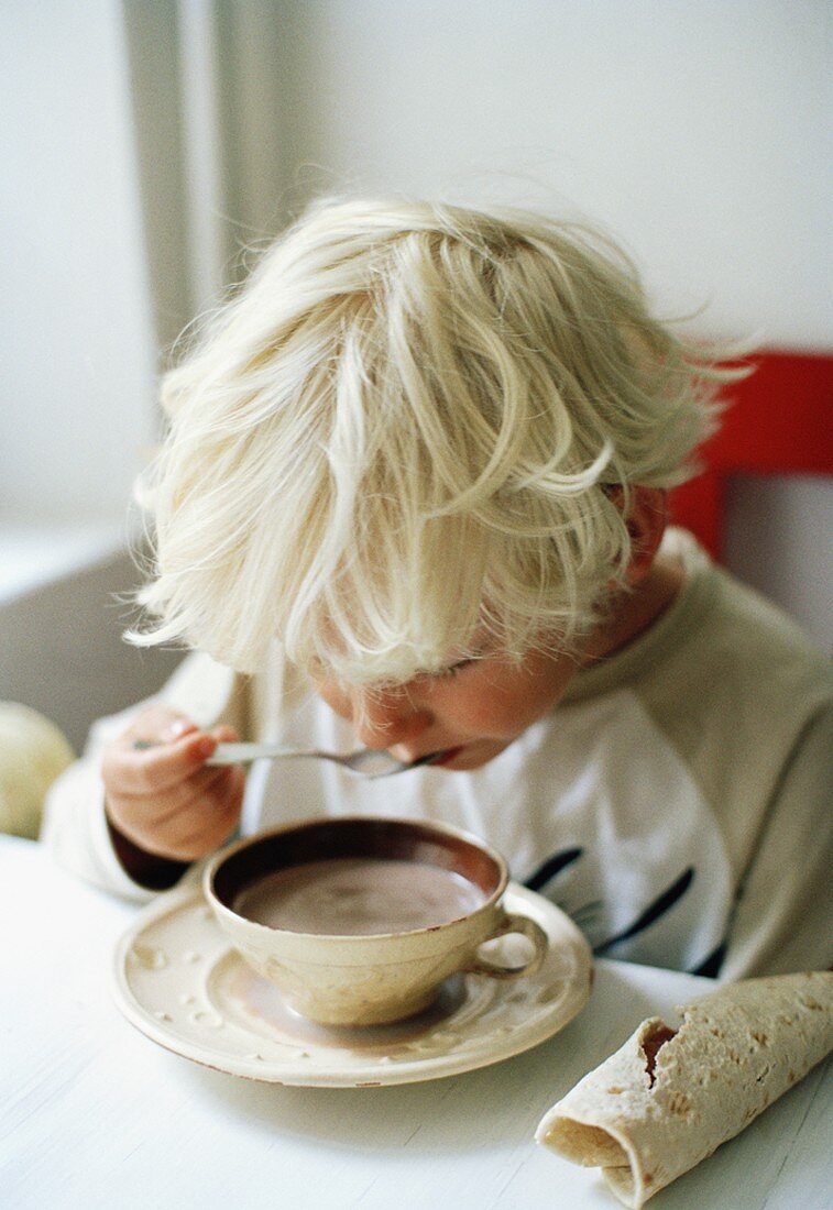 Little boy drinking cup of cocoa with spoon