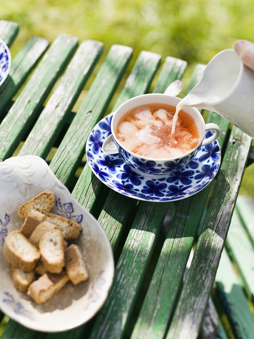 Tee mit Milch und Gebäck auf Gartentisch