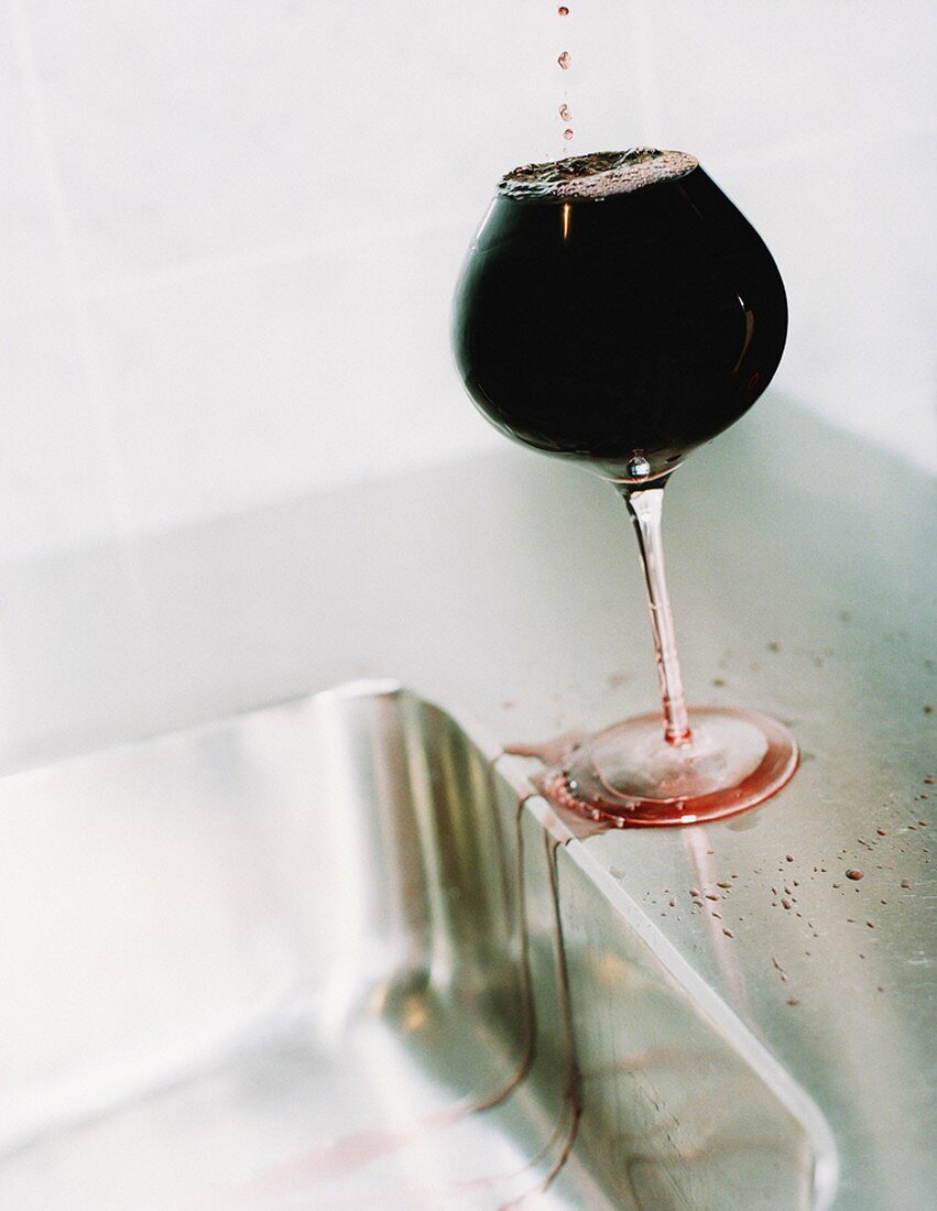 Over-full glass of red wine beside sink