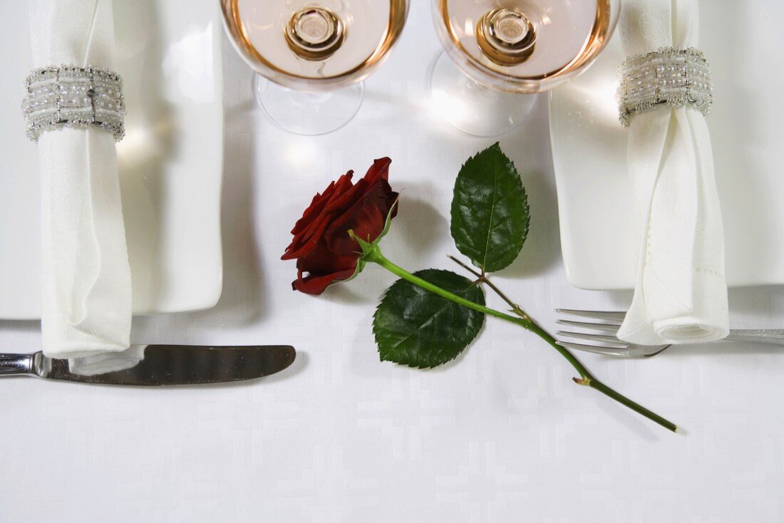 Two place settings for a celebration with champagne glasses and a red rose