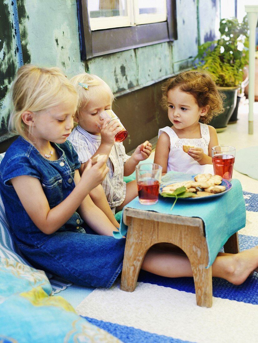 Drei kleine Mädchen mit Plätzchen und Saft auf Terrasse