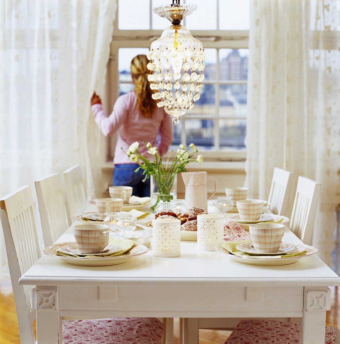 Gedeckter Tisch in Weiß, Frau im Hintergrund am Fenster