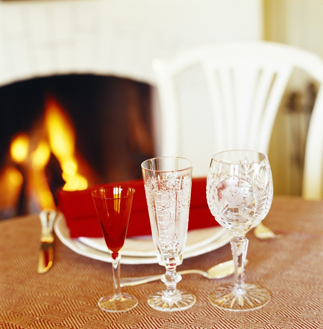Place-setting and crystal glasses on table in front of fire