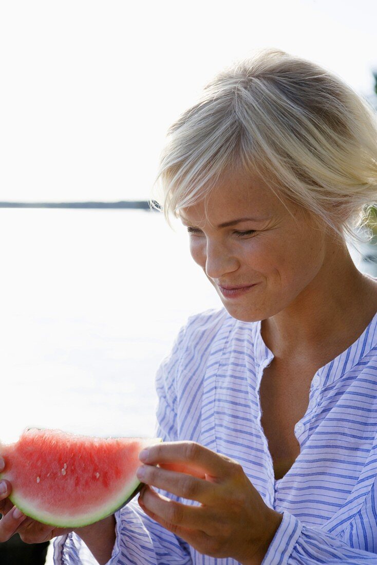 Frau isst Wassermelone am Seeufer