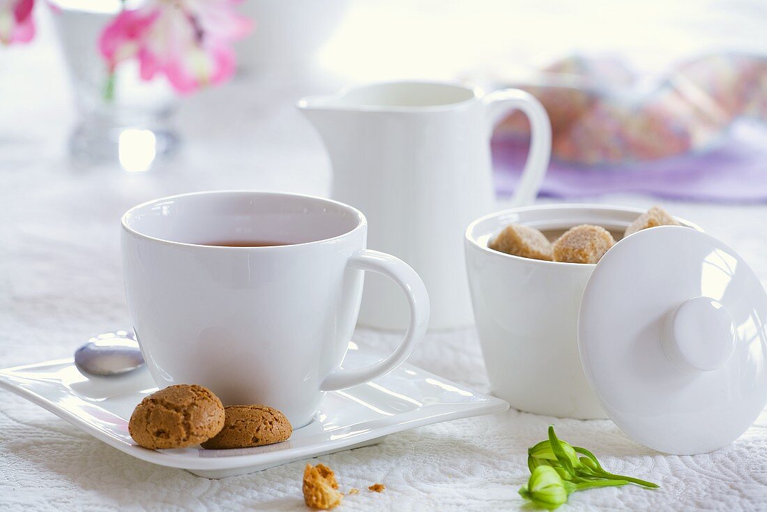 A cup of tea with sugar bowl, milk jug and biscuits