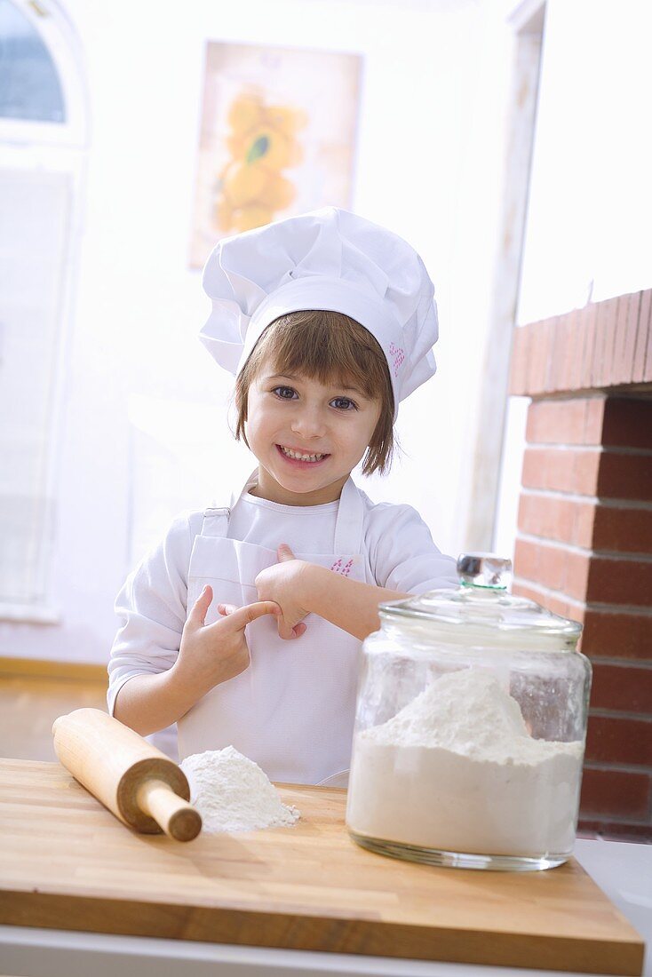 Kleines Mädchen mit Kochhaube, Mehl und Nudelholz