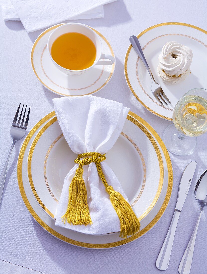 Place-setting with cup of tea, wine and meringue
