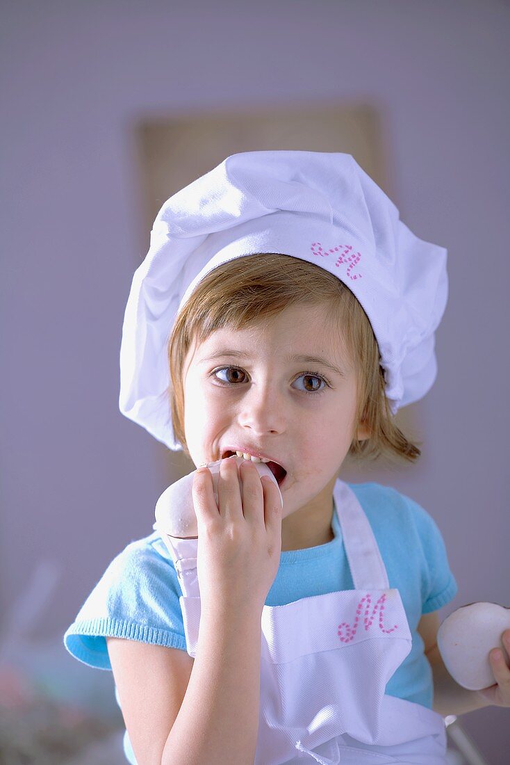 Kleines Mädchen mit Kochhaube isst Lebkuchen