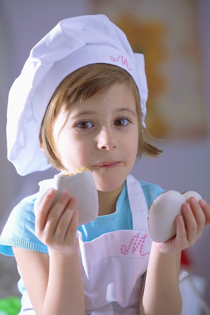 Kleines Mädchen mit Kochhaube isst herzförmige Lebkuchen