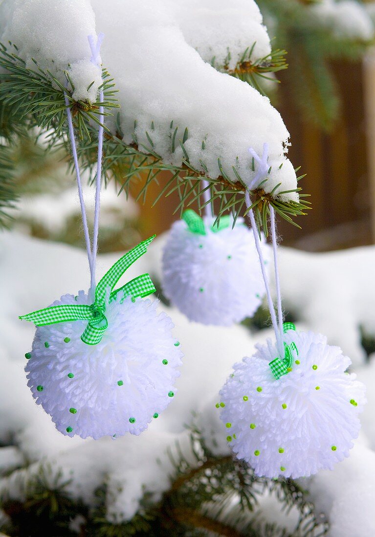 Woll-Schneebälle hängen an verschneitem Tannenzweig