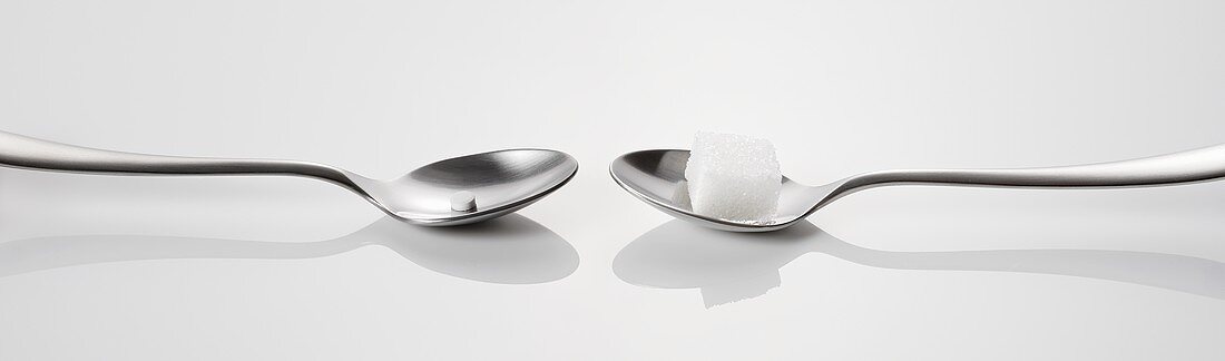 Two spoons, one with a sweetener, one with a sugar cube
