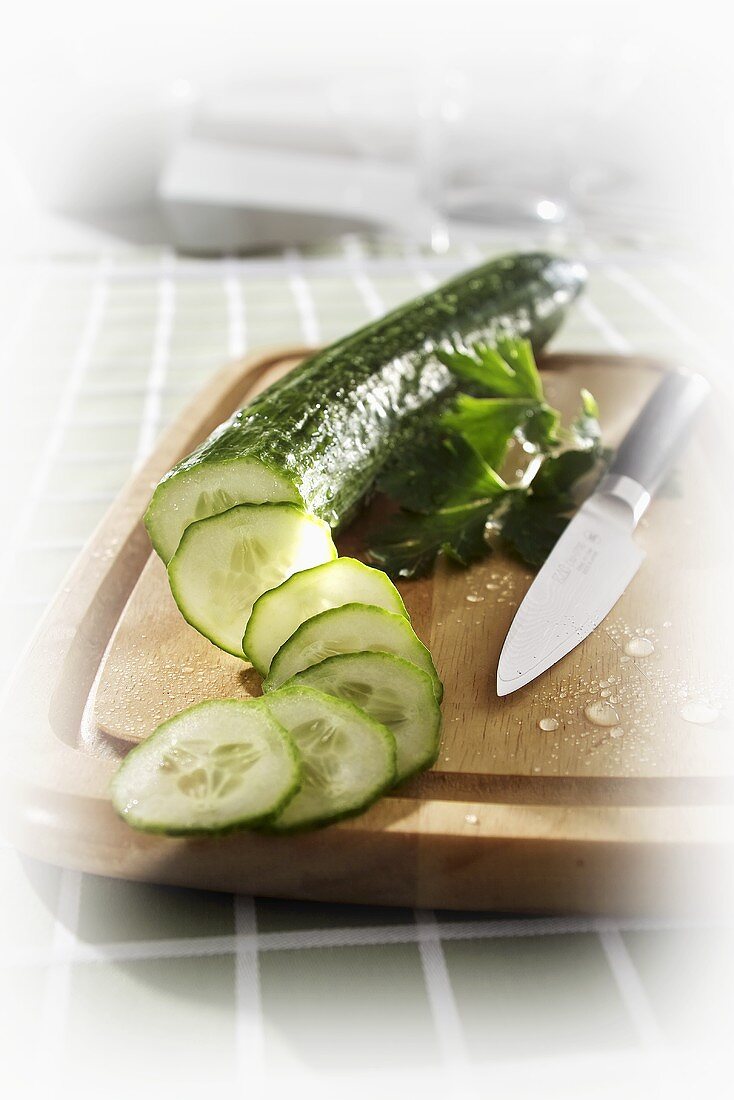 Cucumber, partly sliced, on chopping board