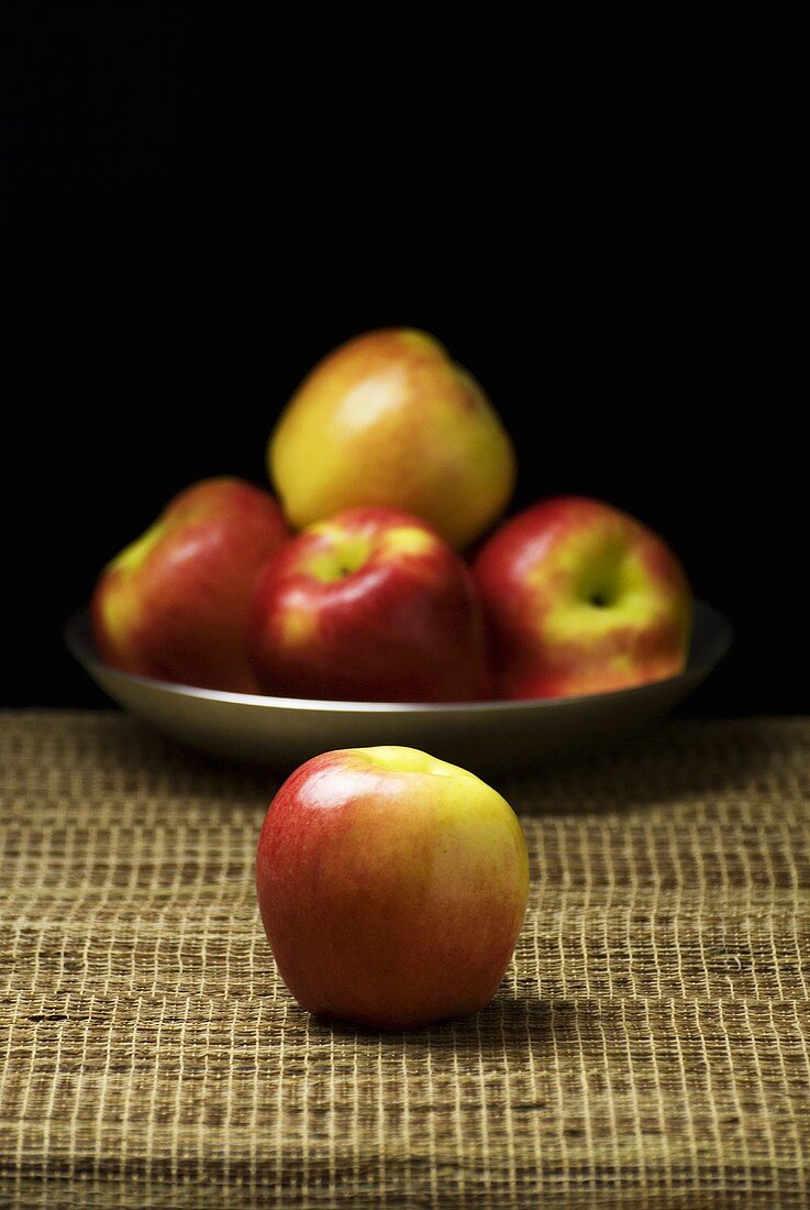 Einzelner Apfel vor einem Teller Äpfel