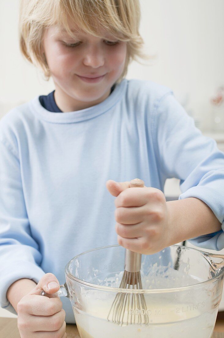 Boy stirring baking mixture in glass bowl with whisk