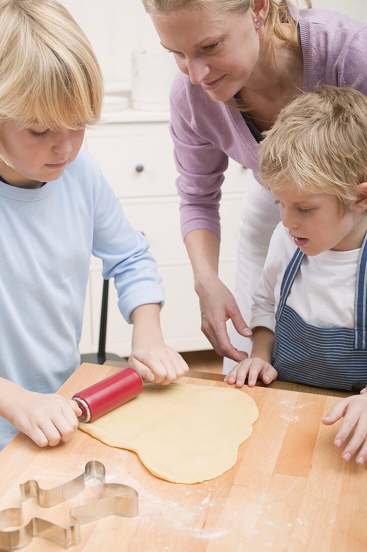 Boy rolling out dough, woman and little boy watching