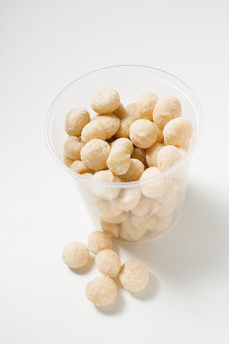 Salted macadamia nuts in and beside plastic tub