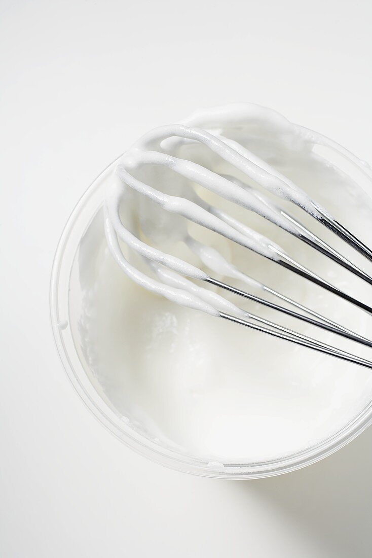 Beaten egg white on whisk and in plastic tub