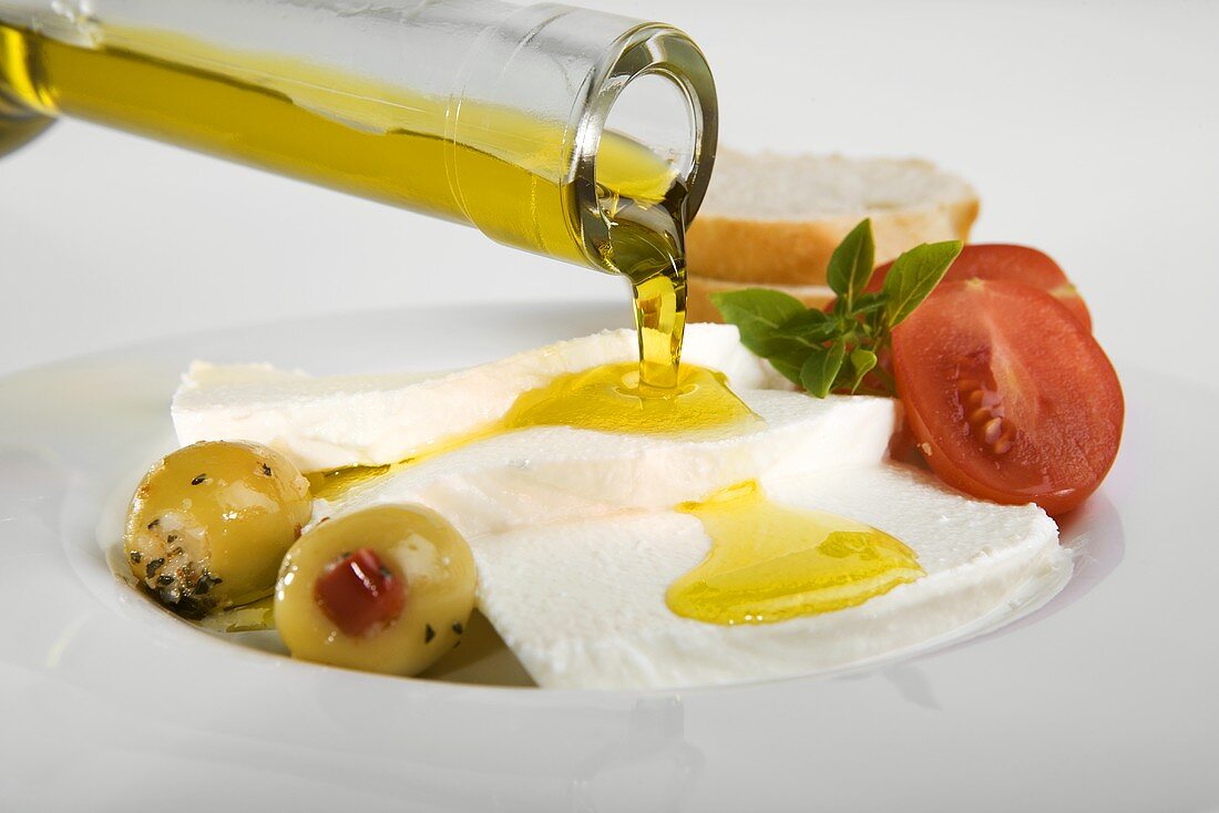 Olivenöl über Ricotta mit Tomaten und Oliven gießen