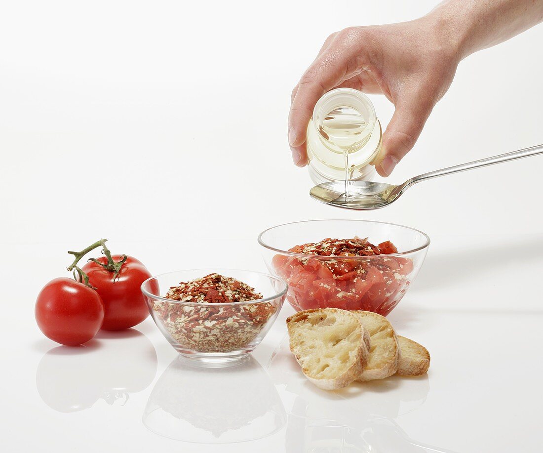 Ingredients for bruschetta, hand pouring oil into spoon