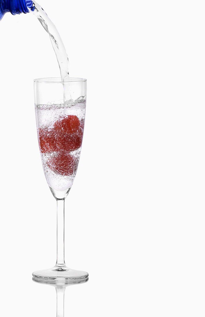 Wasser in Glas mit Himbeeren einschenken