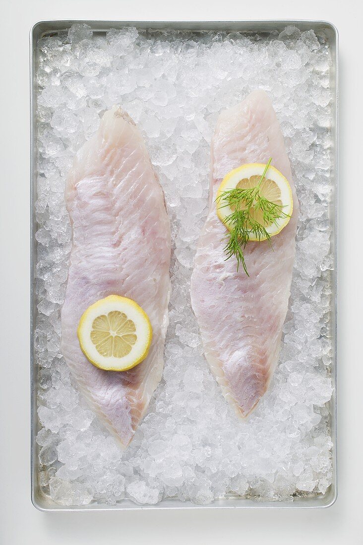 Two fish fillets with slices of lemon on ice