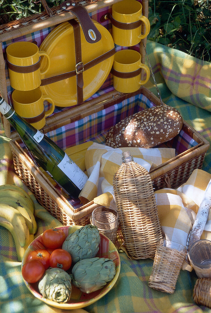 Set of yellow crockery in picnic basket with fruits and vegetables on blanket