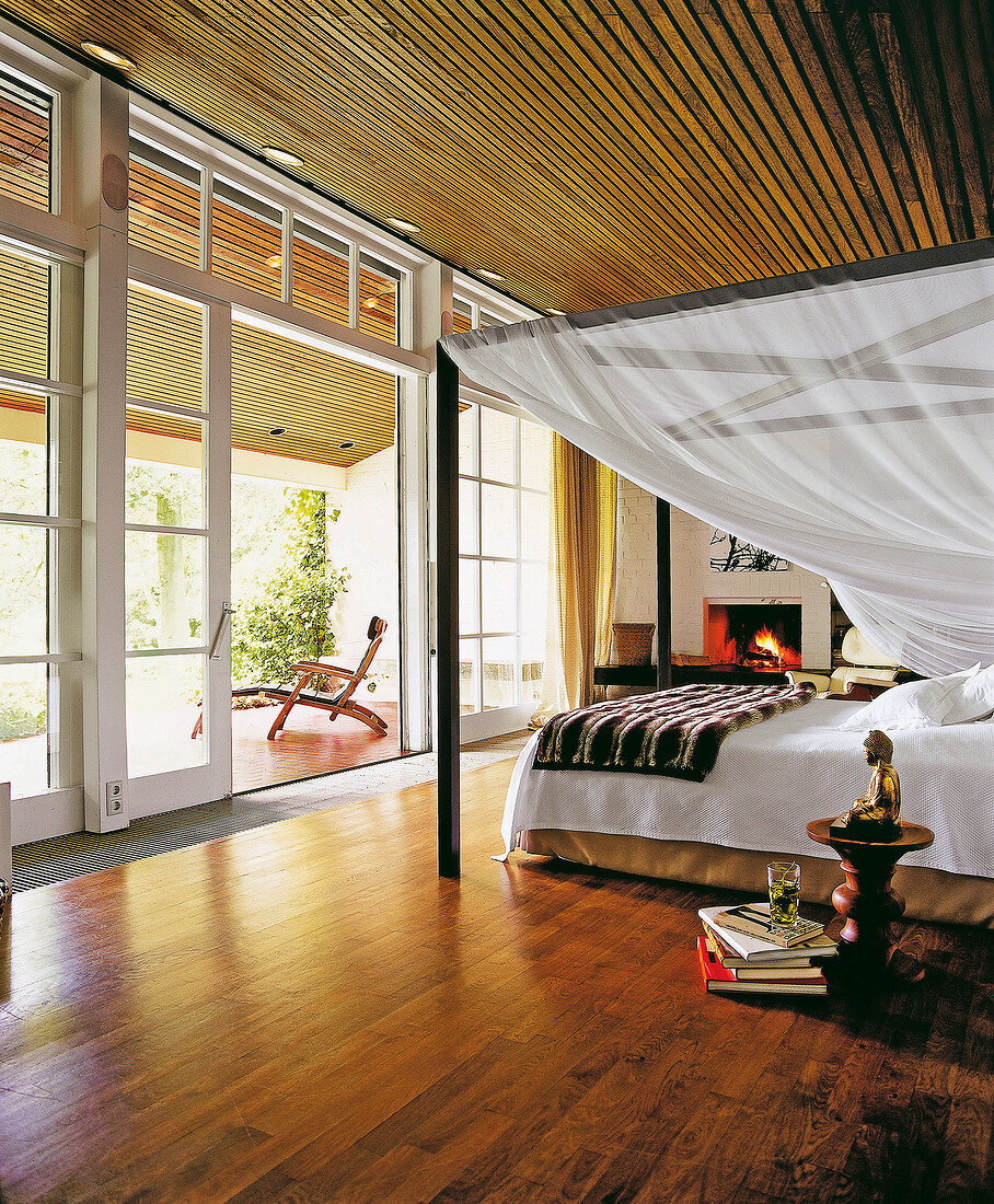 Interiors of bed room with four poster bed in front of fireplace overlooking terrace