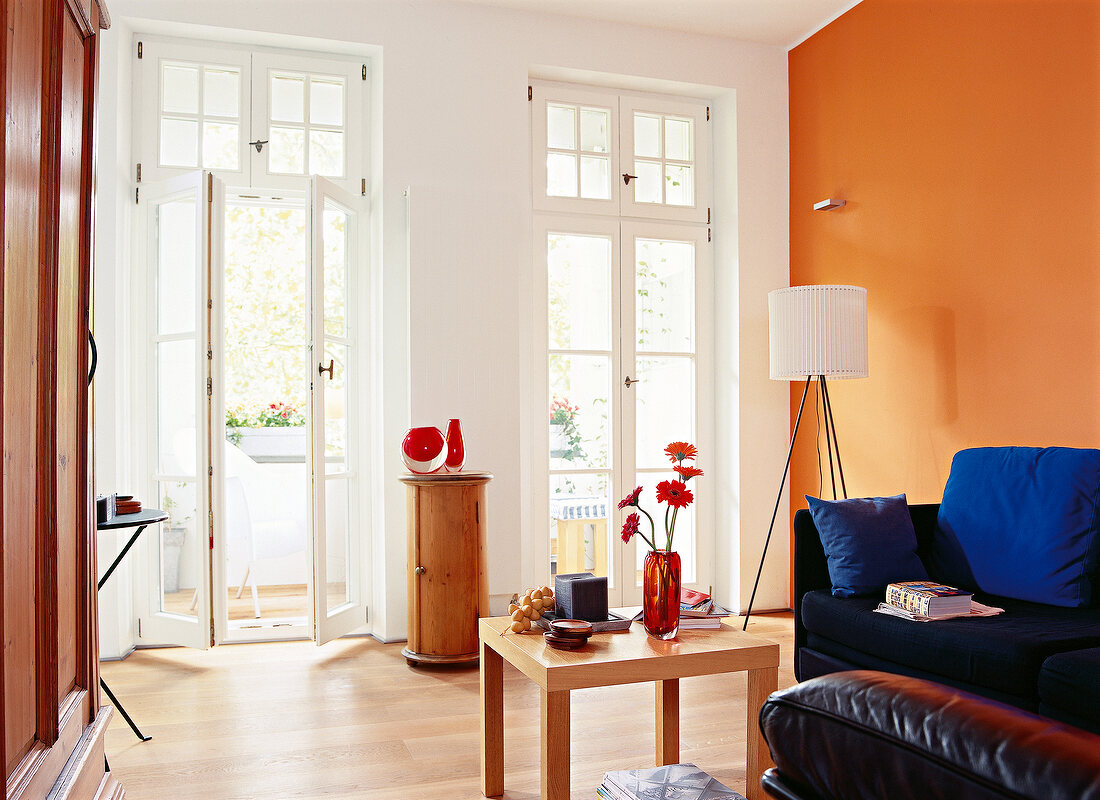 Wohnzimmer mit Wänden in weiß und orange, blaues Sofa, Balkontüren