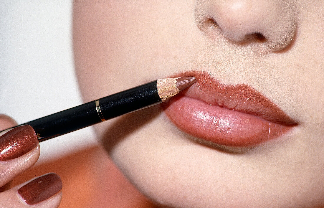 Close-up of woman applying lip liner with pencil