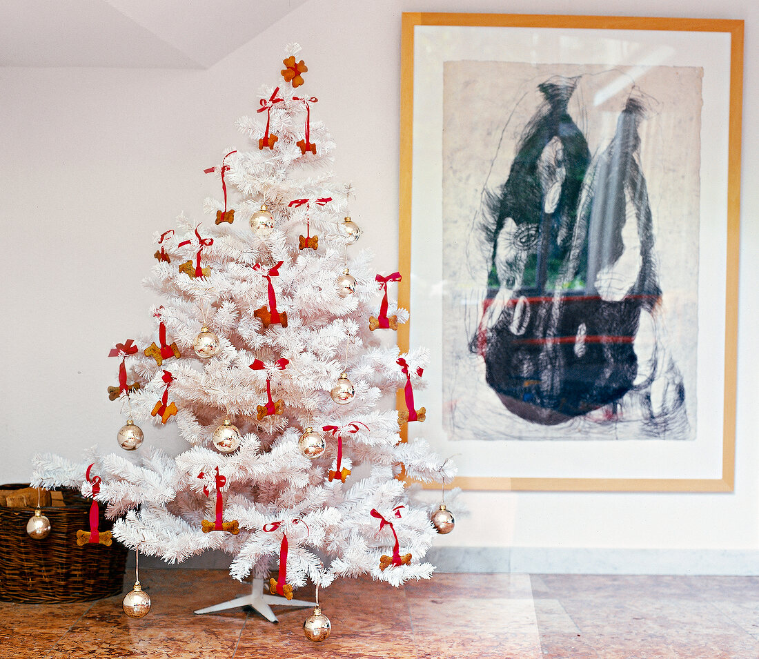 White Christmas tree decorated with baubles and red bows in front of wall painting