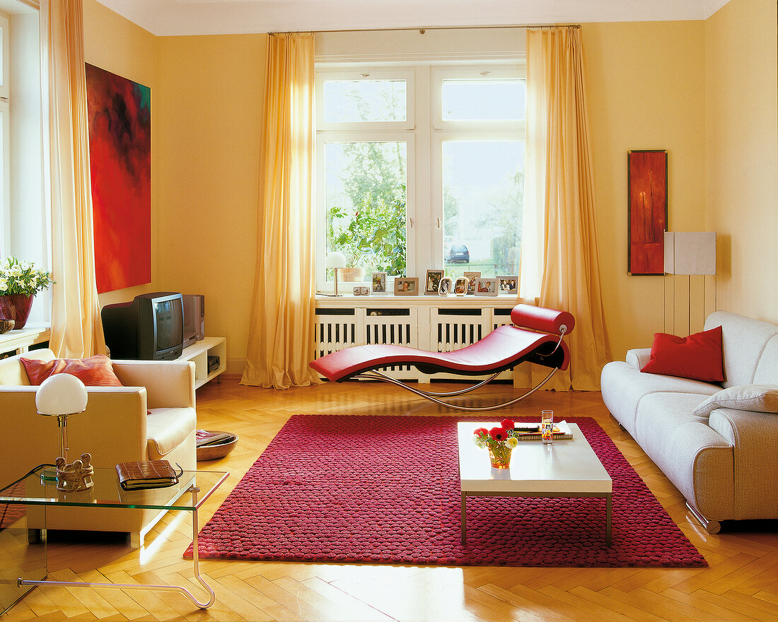 View of living room with red chair lounger, carpet, beige walls, sofa and windows
